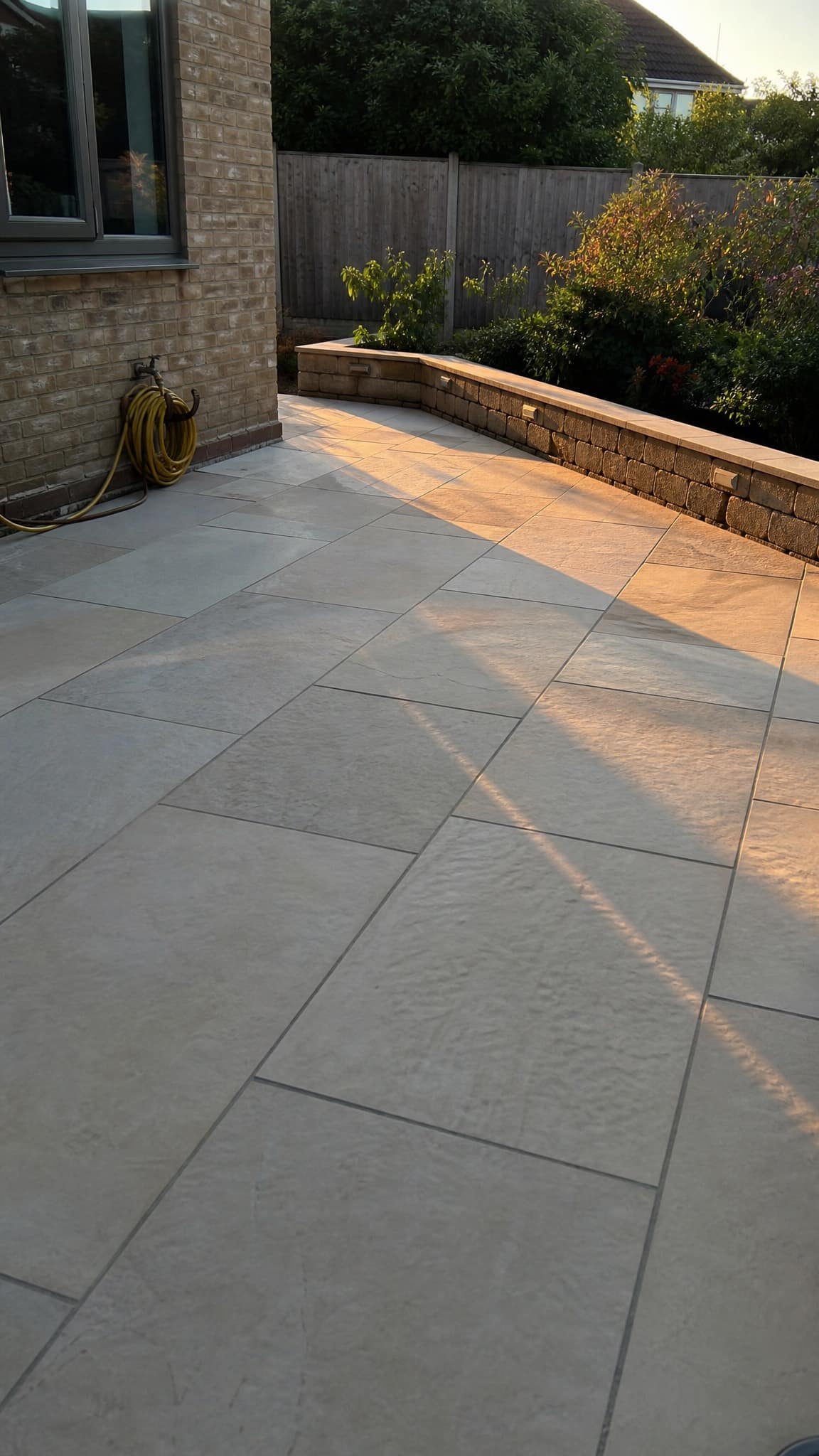 A finished stone terrace at golden hour with a low garden wall